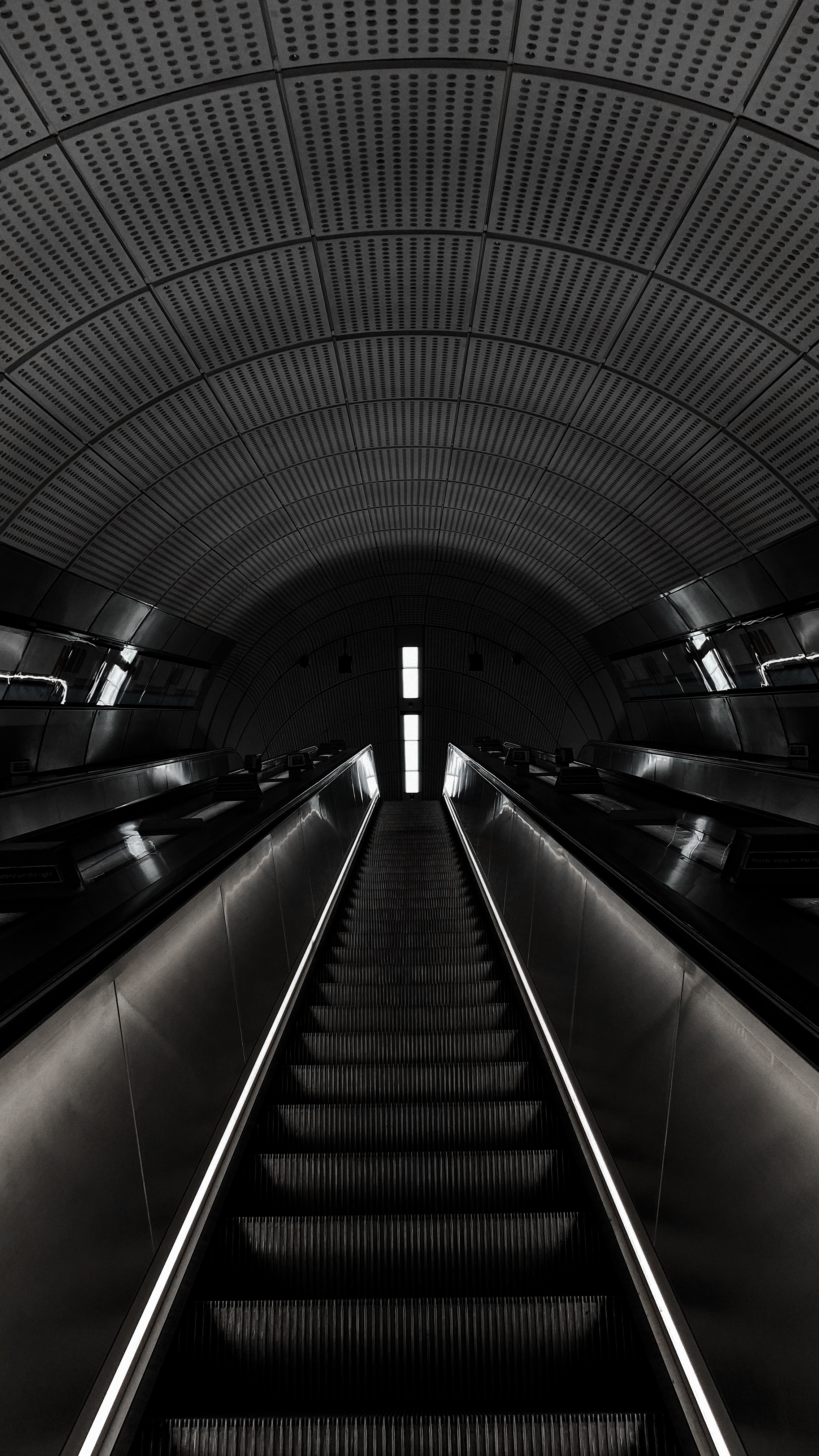 Black-and-white view up an empty escalator beneath a curved perforated ceiling