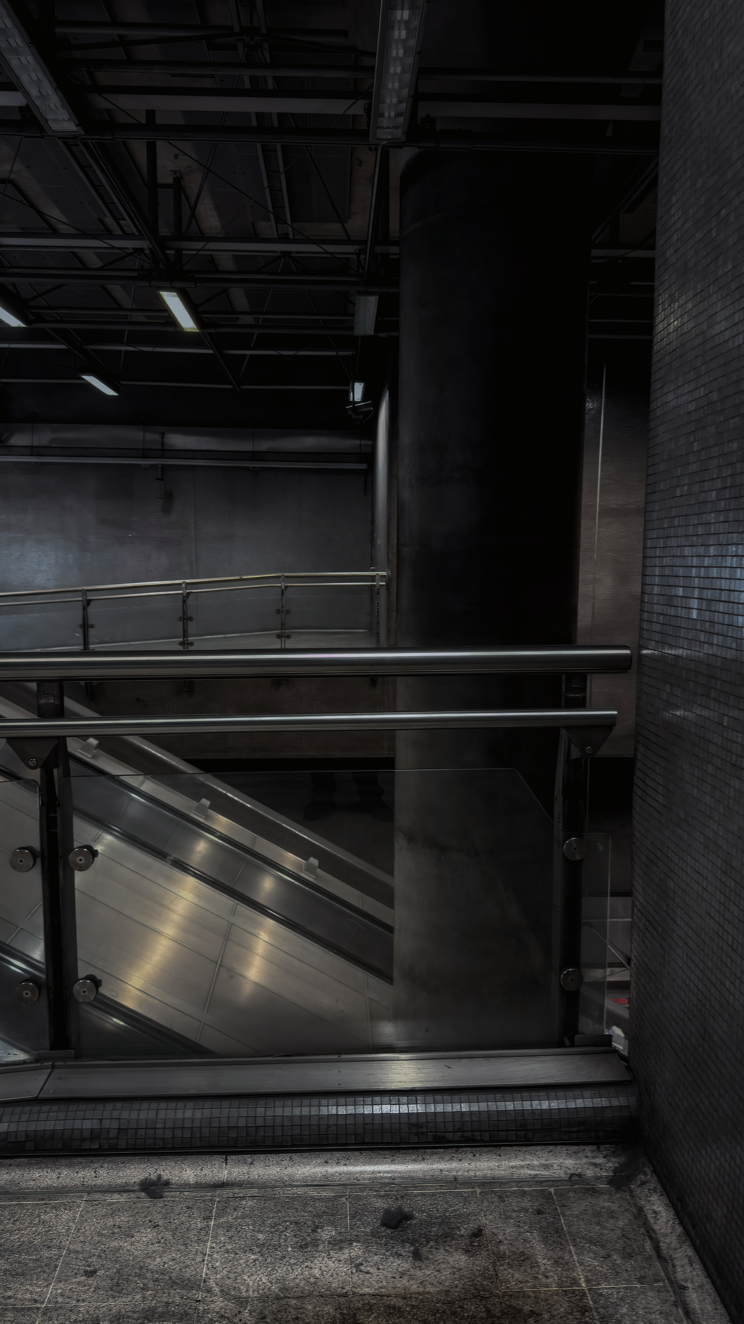 Dark concrete columns and horizontal rails above a reflective escalator at Canada Water