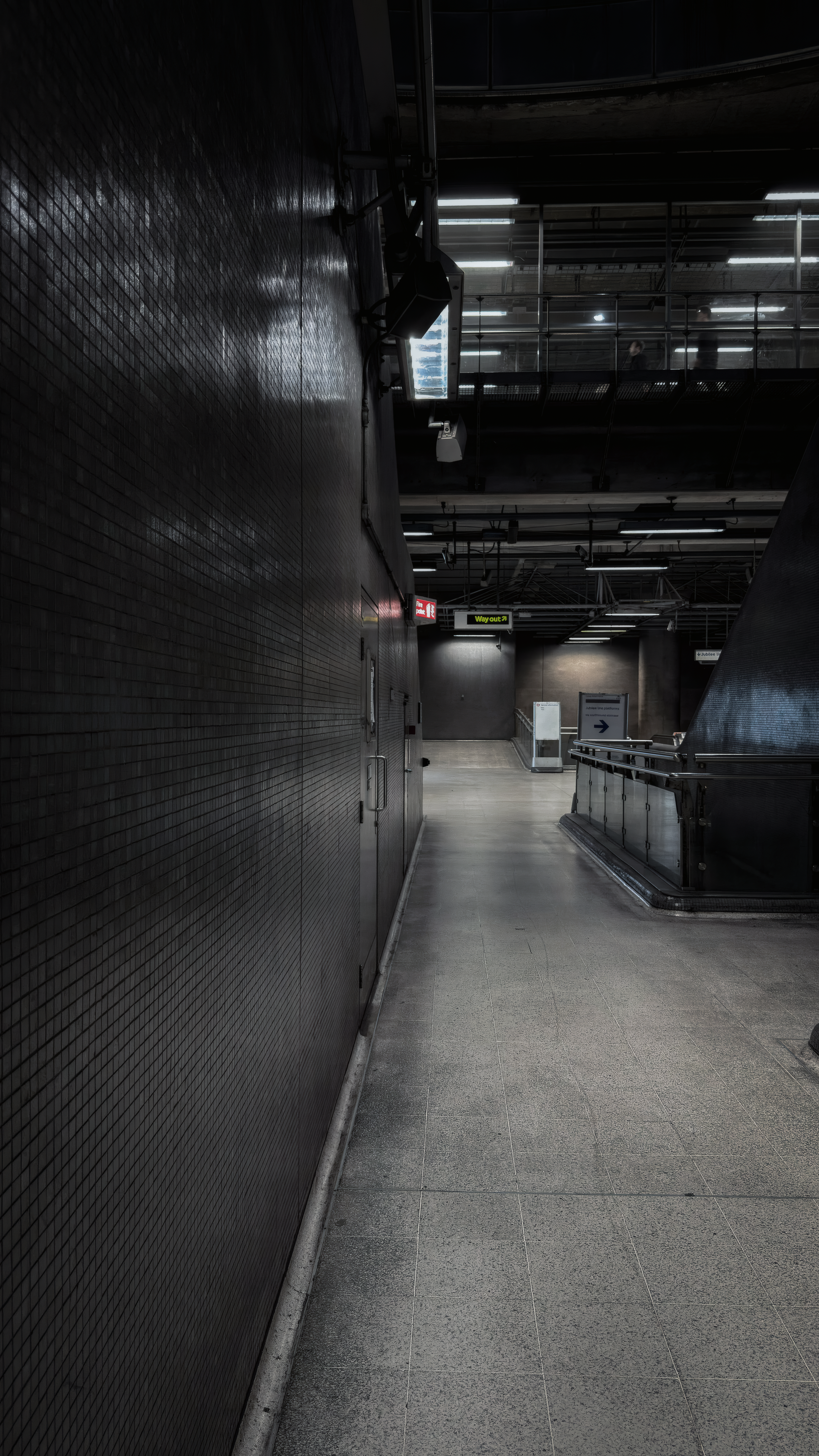 A curved tiled wall leading through an empty passage beneath Canada Water’s exposed steel structure