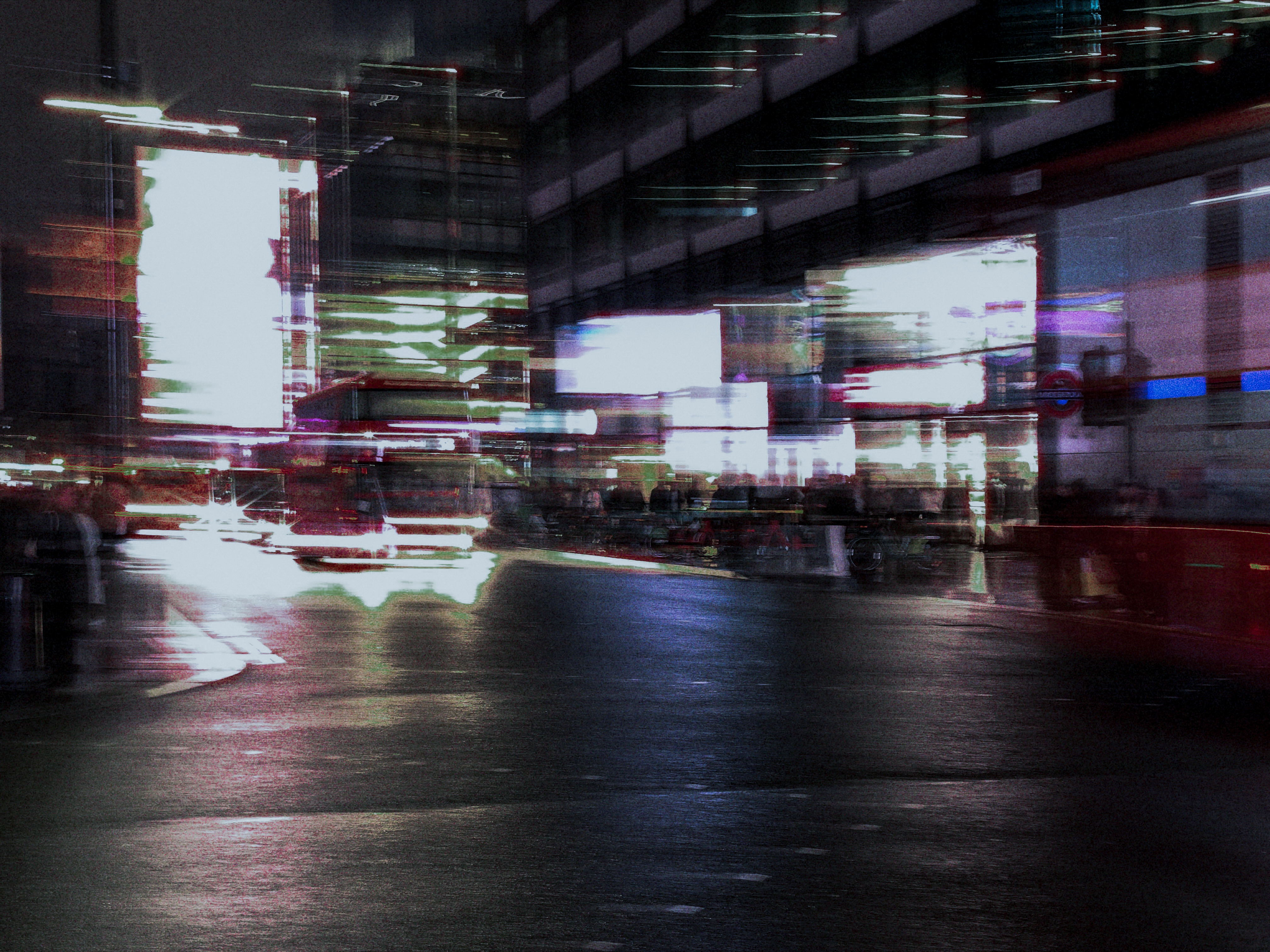 Headlights and illuminated windows streaking across a broad night-time street scene