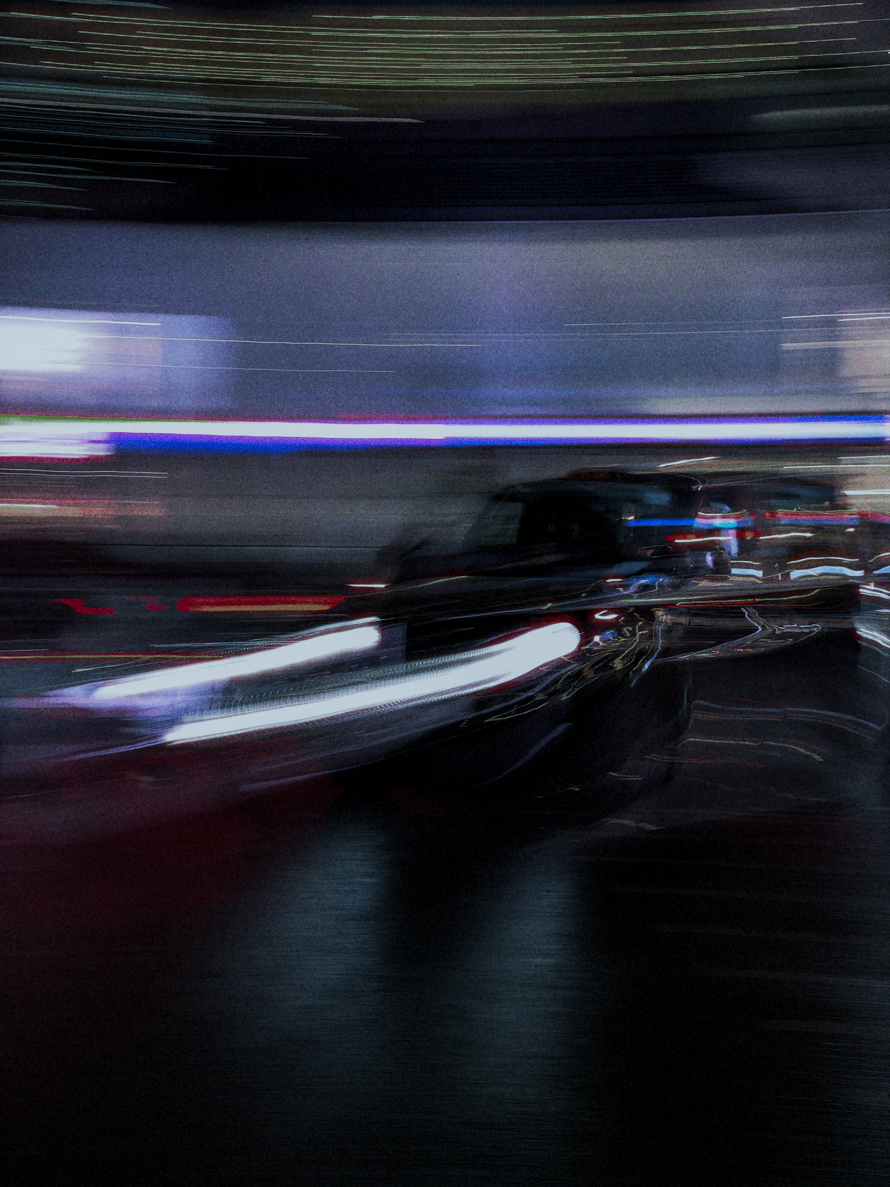 White and violet light trails sweeping past a dark car over reflective asphalt