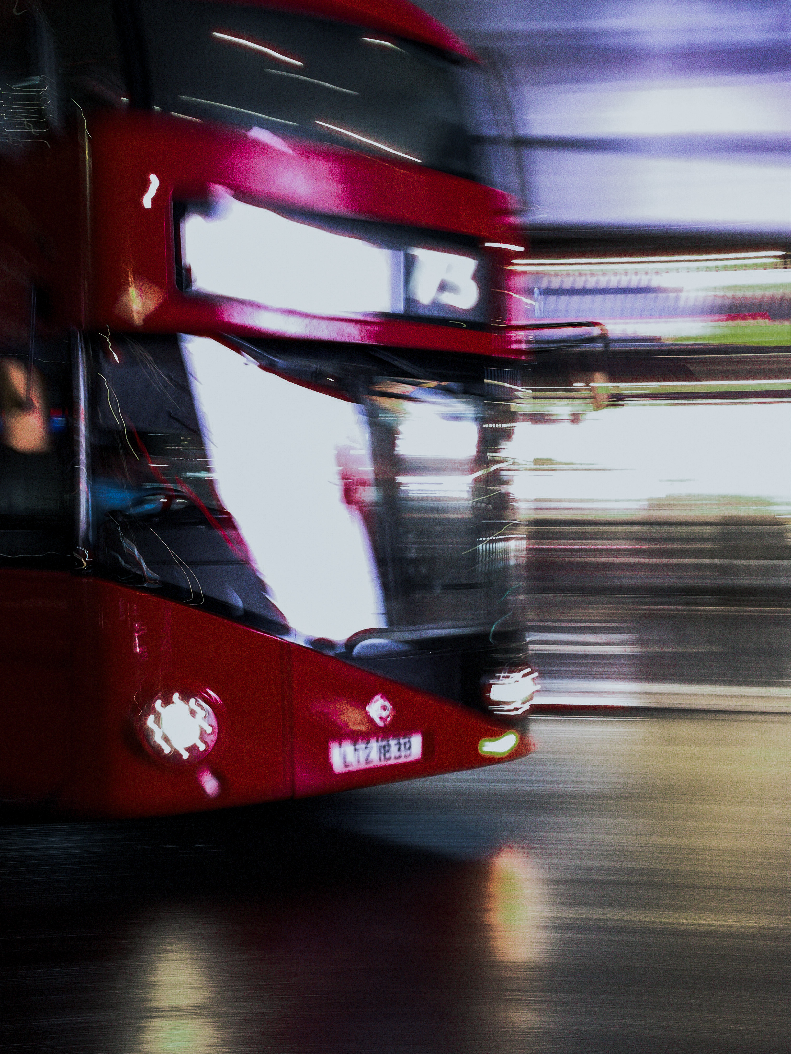 A close view of a passing red double-decker bus softened by motion and reflected light