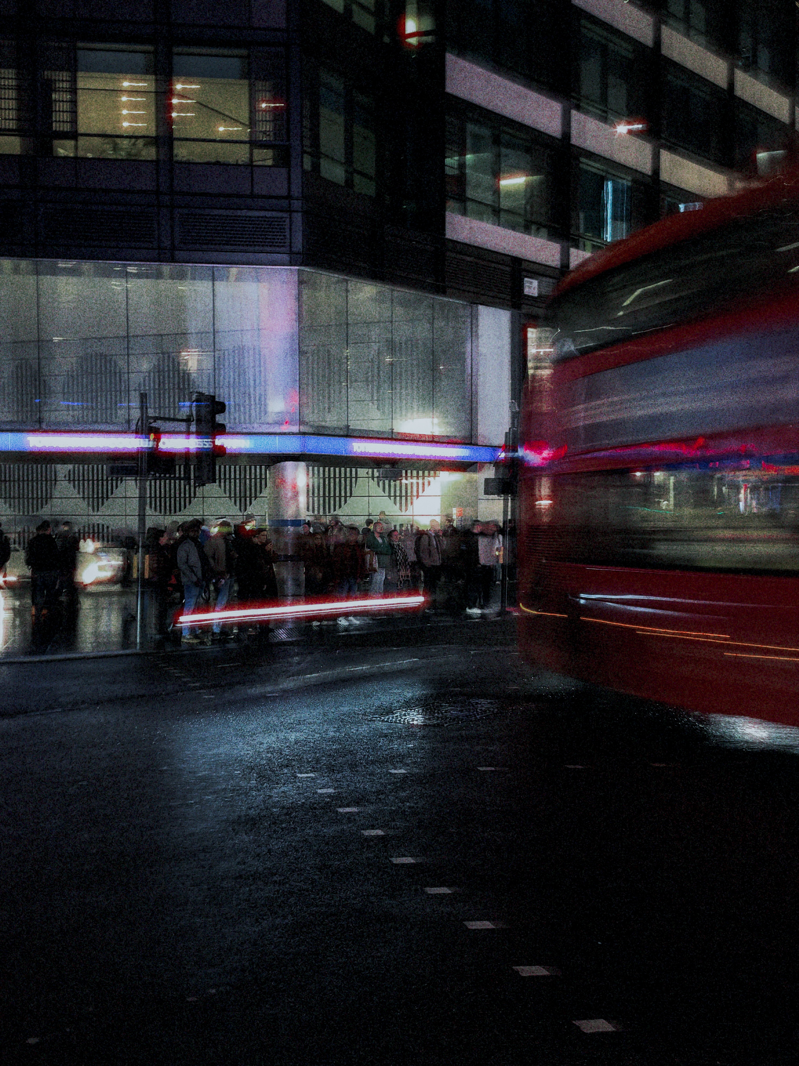 A red bus crossing a wet street beside a lit glass corner building at night