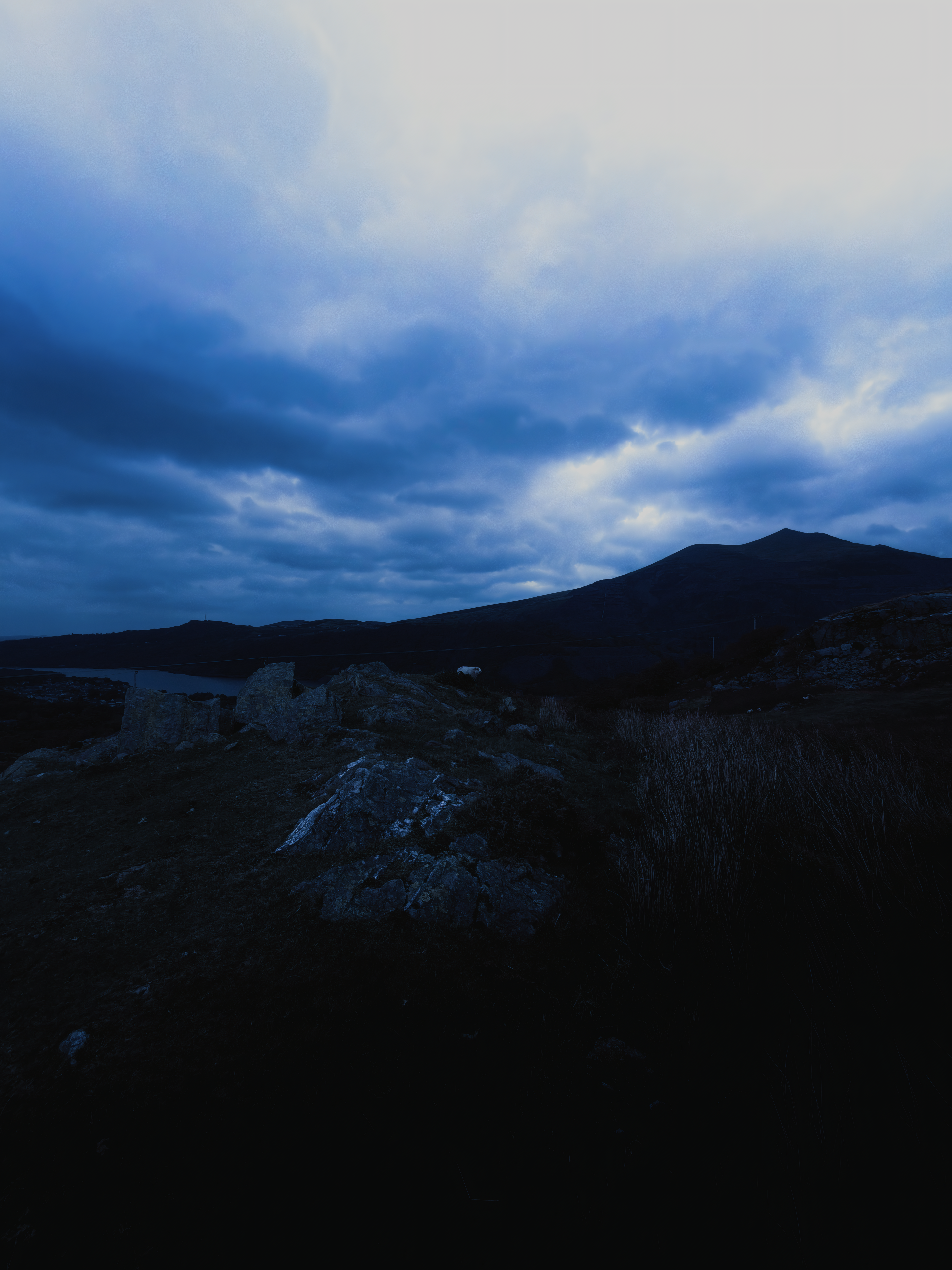 A rocky mountain path beneath layered clouds and an opening of blue sky