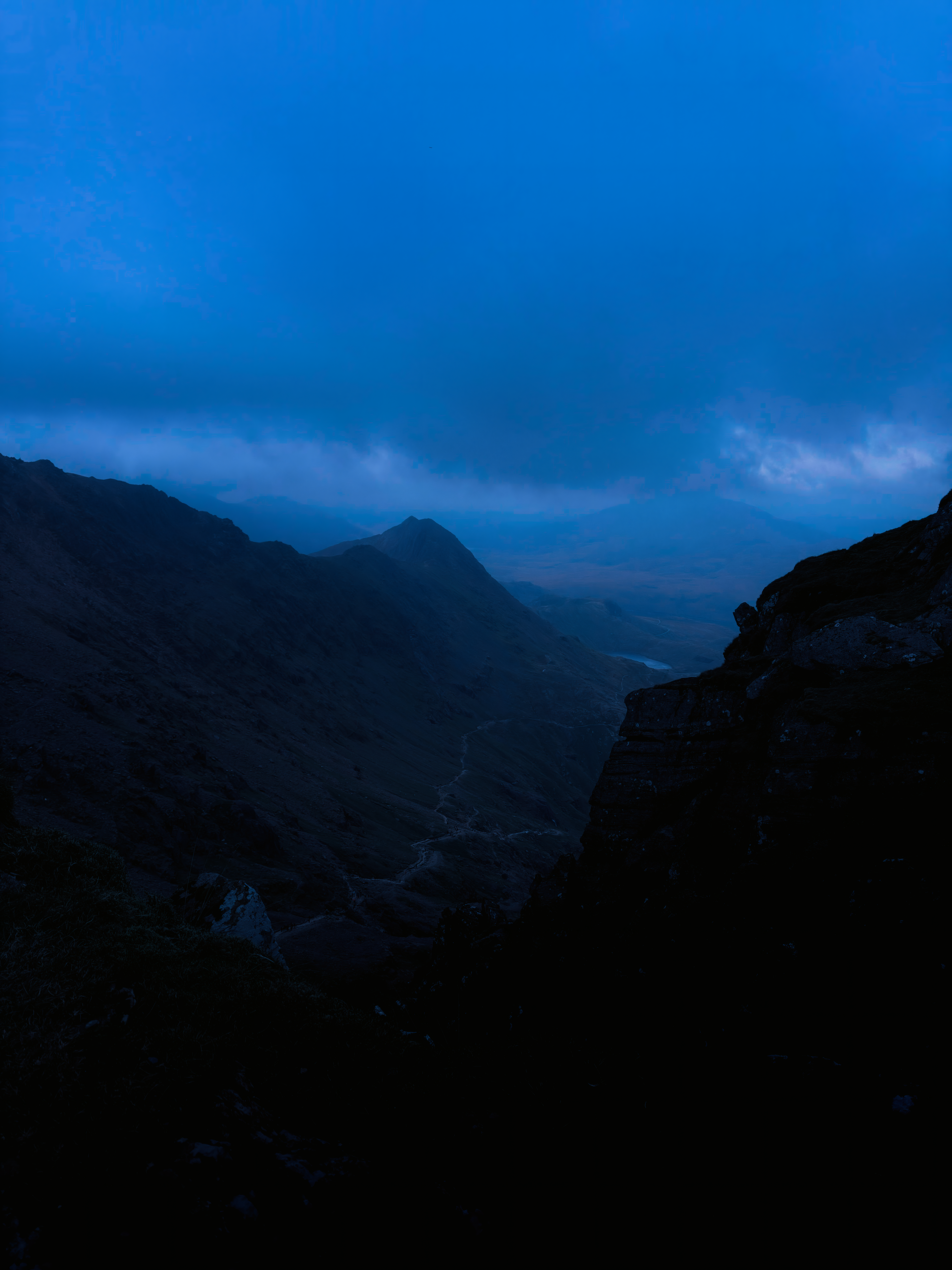 Steep mountain slopes framing a distant valley beneath deep blue clouds