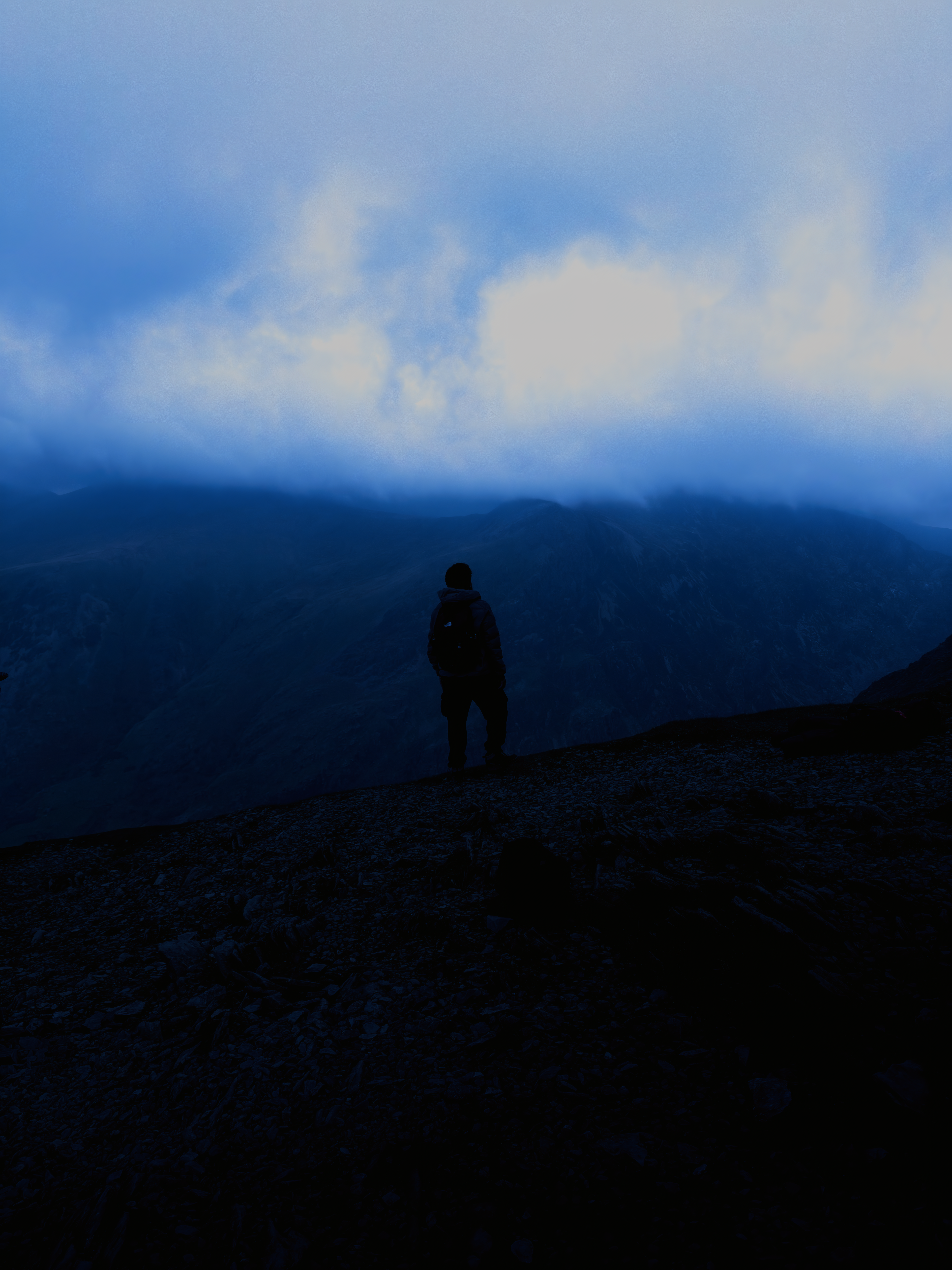 A lone walker silhouetted on a mountain ridge beneath bright cloud