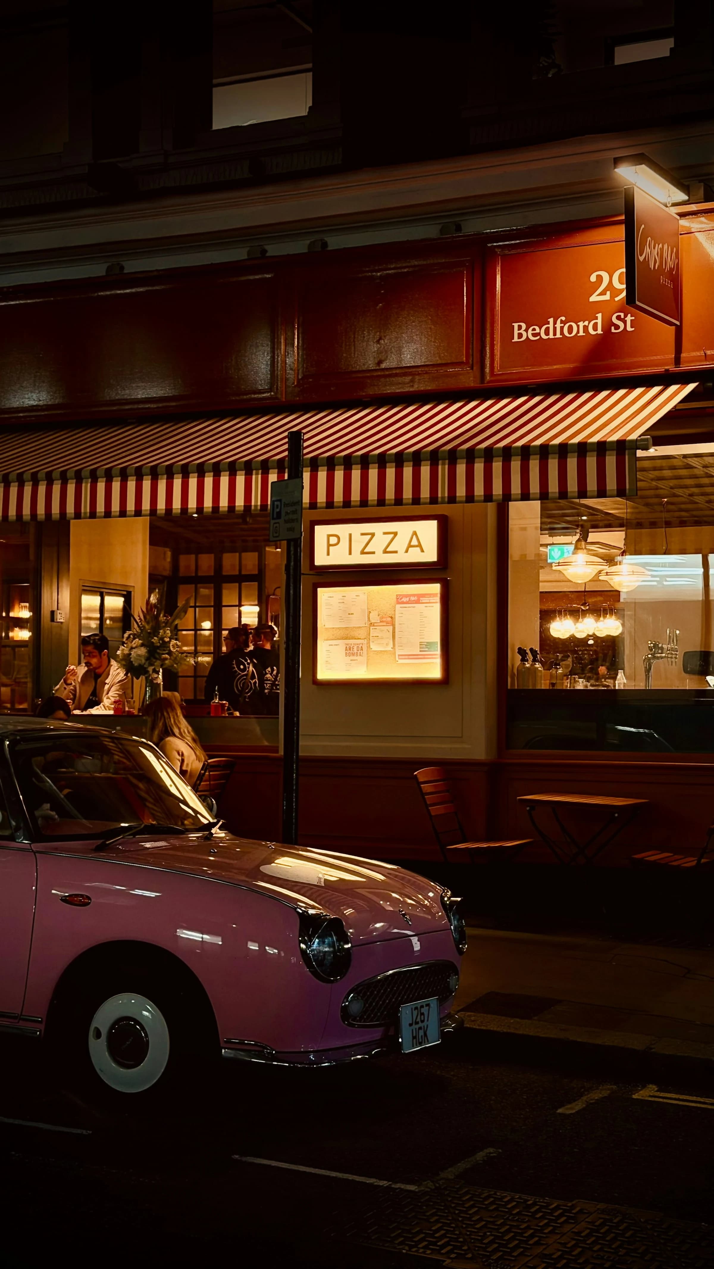 Pink car parked outside a pizza restaurant at night